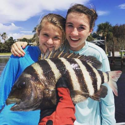 Two girls on a dock, man with red glove holding large fish